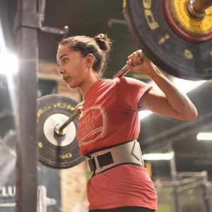 indian woman wearing a weightlifting belt, holding heavy barbell for a squat