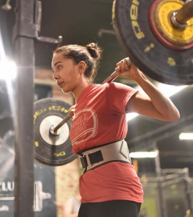 indian woman wearing a weightlifting belt, holding heavy barbell for a squat